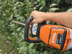 Taille-haie sur batterie STIHL HSA 60 devant une haie photinia eleagnus dans un jardin du Sud