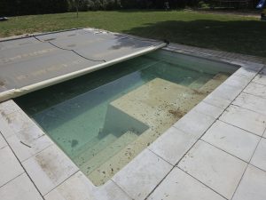 Piscine au printemps après retrait de la bâche d'hivernage, niveau d'eau haut après les pluies d'hiver