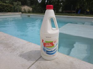 Bidon d'eau de Javel posé au bord d'une piscine pour traitement choc