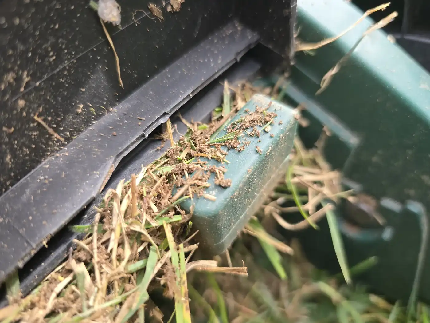 Logement d’accroche du bac du scarificateur Parkside bouché par de l’herbe et de la terre